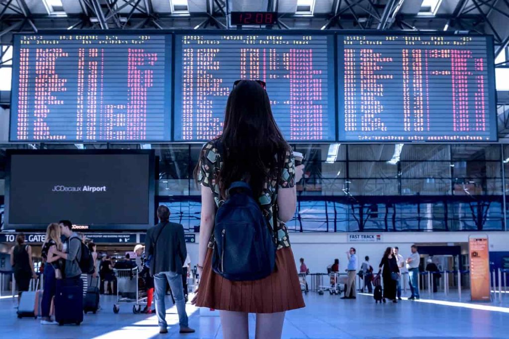 Une femme regarde un panneau d'affichage des vols, de nombreuses personnes se retrouvent coincées dans un aéroport.