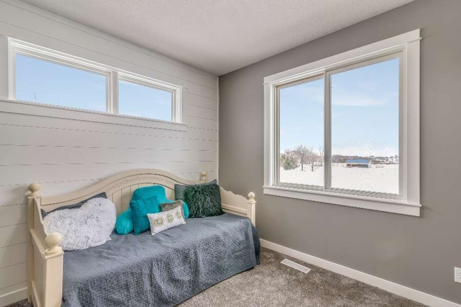 Une petite chambre lumineuse avec un lit daybed gris, des coussins colorés et de grandes fenêtres pour rendre une petite pièce visuellement plus grande.