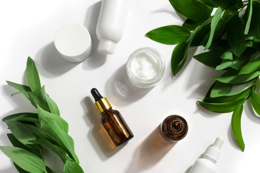 Des produits de beauté bio sont disposés sur un fond blanc, entourés de branches de verdure pour souligner leur origine naturelle.