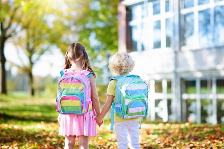 Deux jeunes enfants avec des cartables colorés se tiennent la main pour leur rentrée en maternelle.