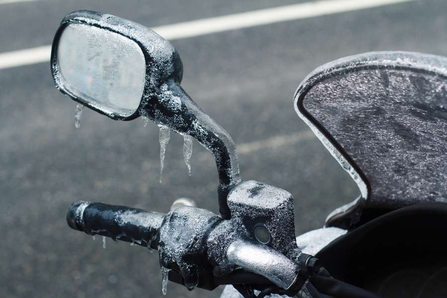 Un rétroviseur et un pare-brise teinté de moto complètement recouverts par une couche de givre et de glace.