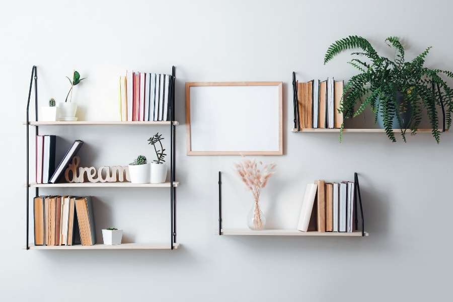 Des étagères murales fixées sur un mur blanc et décorées de livres et de plantes vertes rappelant l'effet d'étagères murales invisibles.