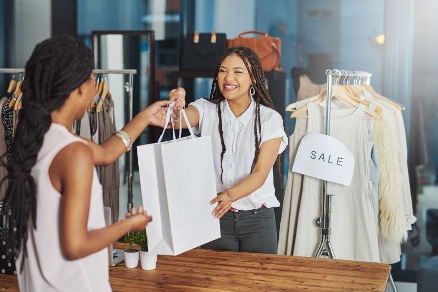 Une commerçante sourit en remettant un sac d'achats à une cliente dans une boutique de vêtements.